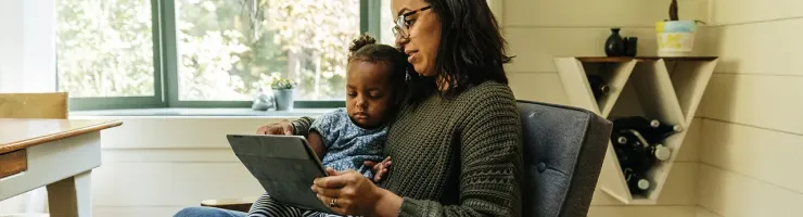 Une femme et un enfant assis sur une chaise, utilisant une tablette ensemble.