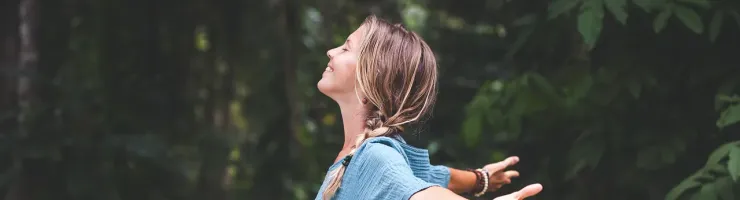 Une femme en robe bleue se tient dans les bois, entourée d'arbres verdoyants.