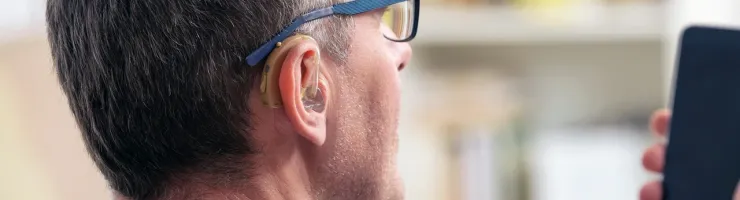 Un homme portant des lunettes et un appareil auditif tenant un smartphone dans sa main.