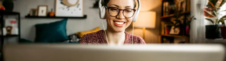 Une femme souriante portant des écouteurs, utilisant un ordinateur portable.