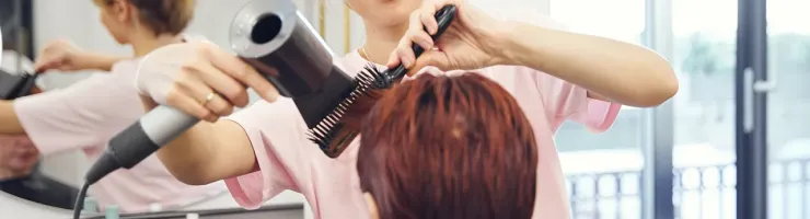 Coiffeuse coiffant une cliente aux cheveux roux dans un salon de coiffure.