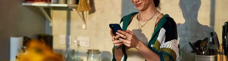 Une femme utilise son téléphone dans une cuisine moderne, entourée d'ustensiles et d'ingrédients.