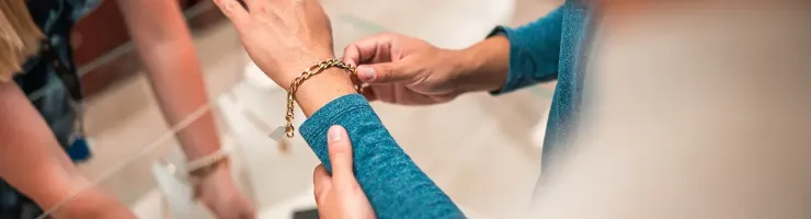 Une femme met un bracelet avec l'aide d'un homme, tous deux souriants dans un cadre chaleureux.