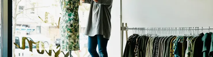 Une femme se tient devant une fenêtre, avec une robe accrochée au mur à côté d'elle.