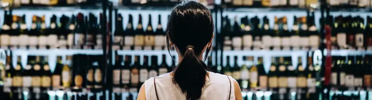 Une femme examine des bouteilles de vin dans un magasin, réfléchissant à son choix.