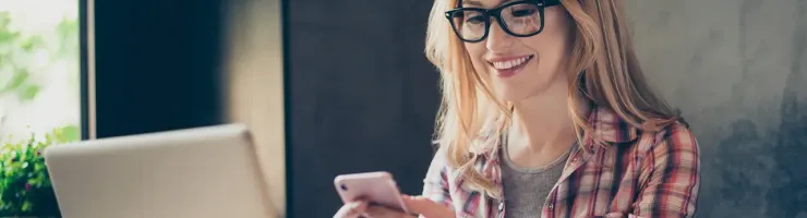 Femme devant un ordinateur portable tenant son smartphone dans la main.