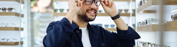 Un homme examine des lunettes dans un magasin, réfléchissant à son choix.