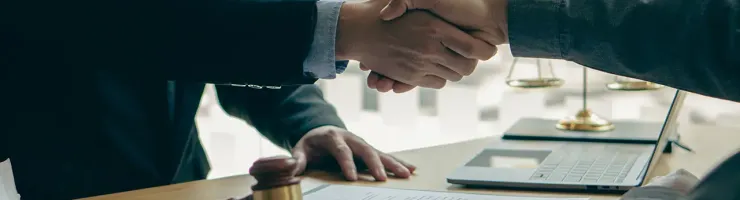 Deux personnes se serrent la main au-dessus d'un bureau avec un ordinateur portable.