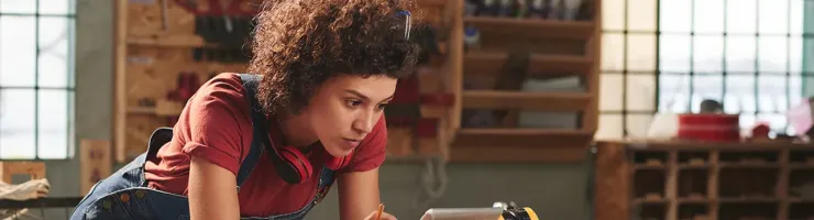 Une femme travaille sur une tablette, entourée d'outils dans un atelier.