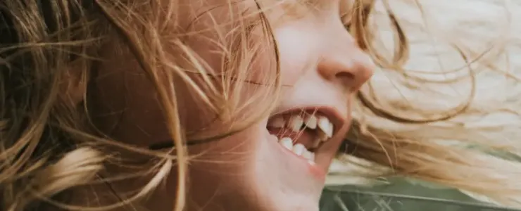 Gros plan sur une petite fille aux cheveux blonds qui rit joyeusement, la tête sortie de la fenêtre d'une voiture.