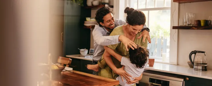 Une famille rit et joue joyeusement dans une cuisine moderne et lumineuse aux meubles vert sombre et bois.