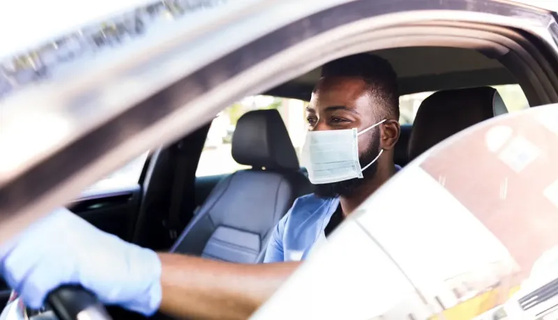 Conducteur portant un masque dans une voiture, respectant les consignes sanitaires.