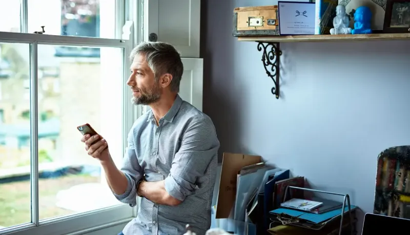 Un homme discute avec une personne via son téléphone portable dans un salon lumineux.