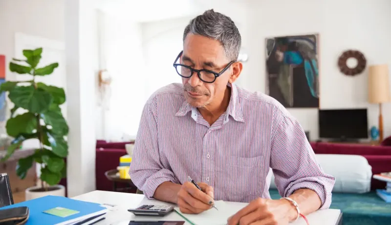 Homme d'âge moyen avec des lunettes prend des notes à son bureau.