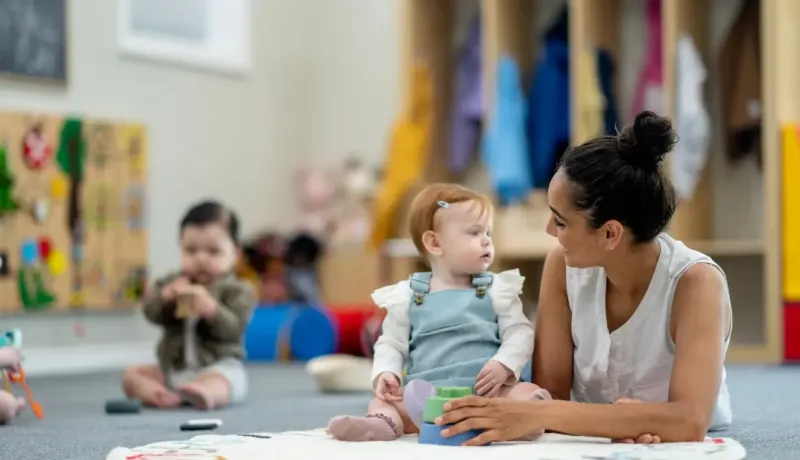 Une agent territorial spécialisée des écoles maternelles aide un bébé à jouer .