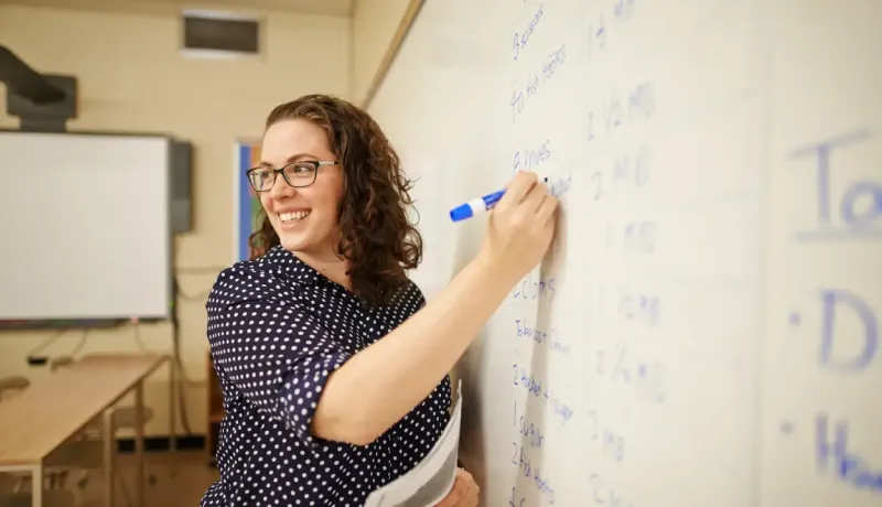 Une femme écrit sur un tableau blanc lors d'un cours.