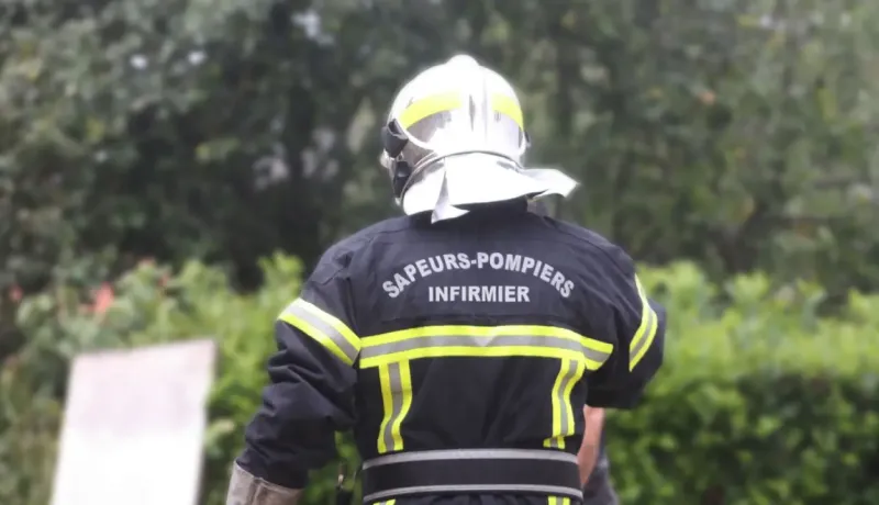 Un pompier vu de dos marche dans une zone boisée, équipement de secours complet.