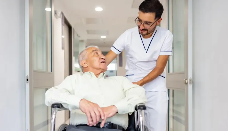 Un infirmier pousse le fauteuil roulant d'une personne âgée dans un hôpital.