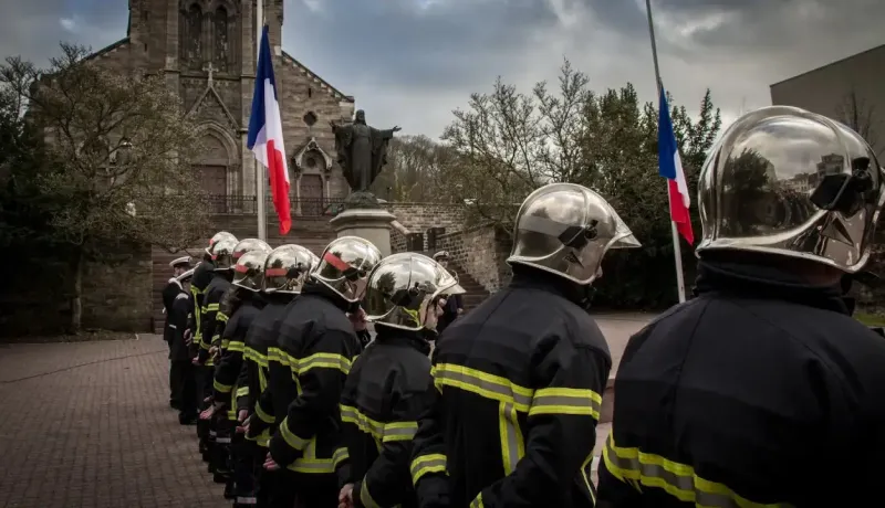 Des pompiers en uniforme, drapeaux français en berne