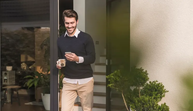 Un homme sort d’un immeuble, tenant un smartphone et une tasse de café.