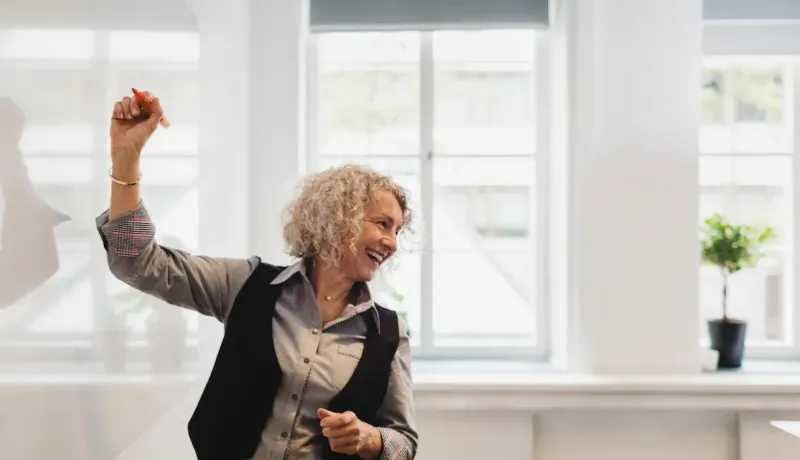 Une institrice souriante prêt à écrire sur un tableau blanc. Elle regarde les élèves.