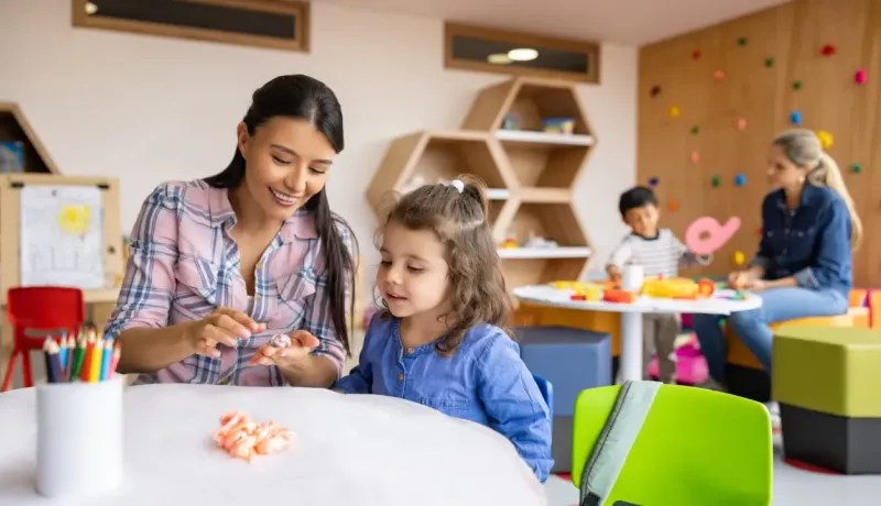Une maitresse d'école montre à une élève comment faire de la pâte à modeler