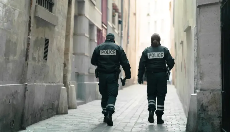 Deux policiers en uniforme marchent dos à la caméra dans une ruelle étroite.