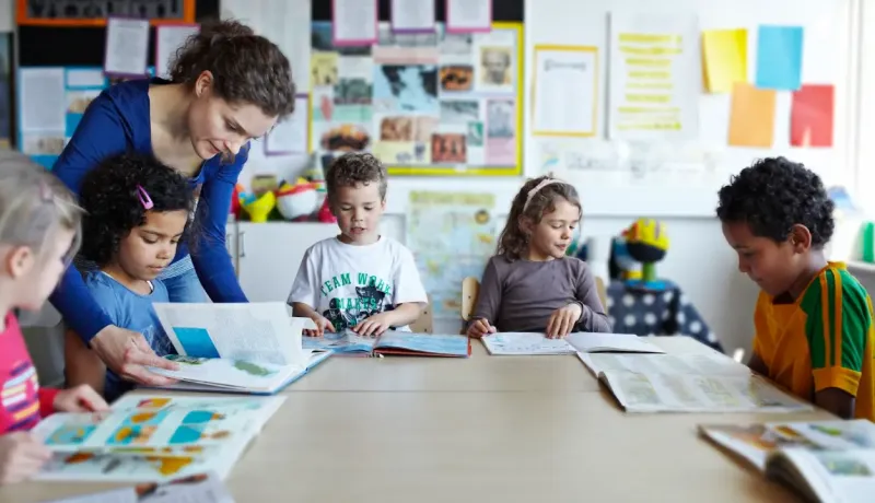 Une maitresse d'école aide une jeune fille à trouver une page d'un livre.