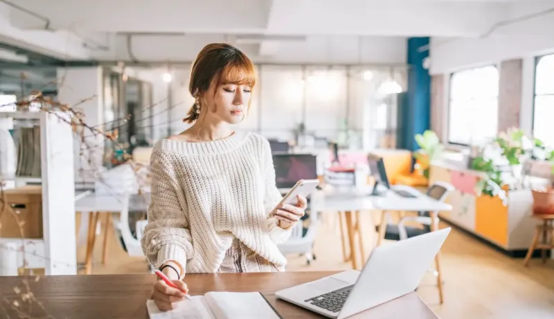 Femme regarde son téléphone et prend des notes