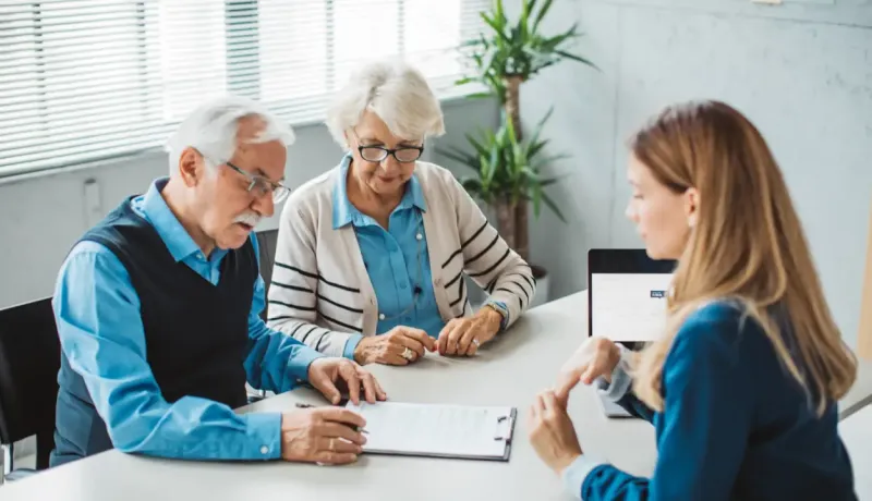 Couple âgé examine des documents avec une jeune femme à un bureau