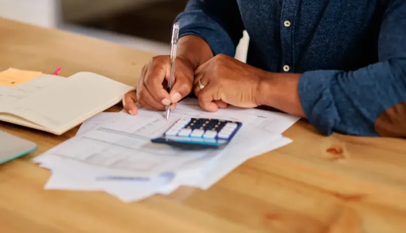Une femme fait ses comptes en inscrivant les résultats obtenus avec une calculatrice.
