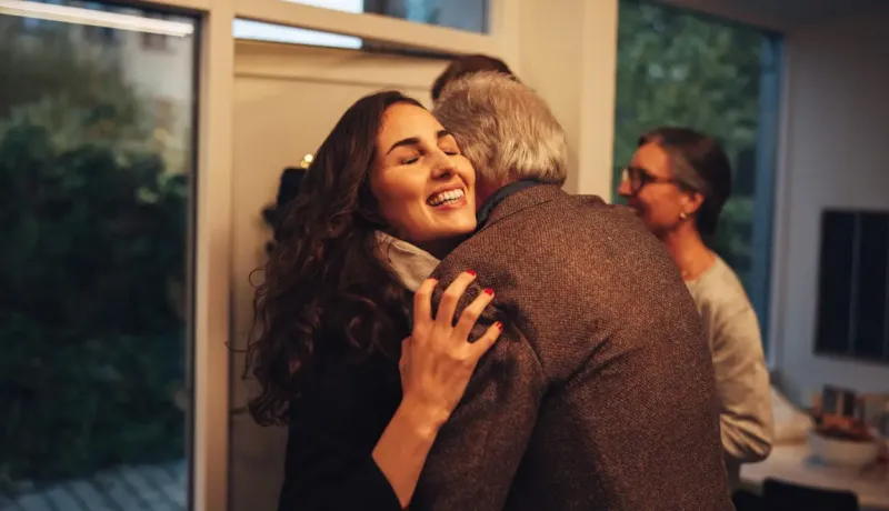 Une fille et son père se font un calin devant l'entrée de la maison.