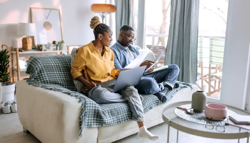 Couple assis sur un canapé, regardant des papiers et un ordinateur portable.