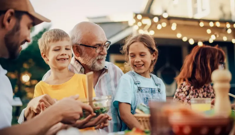 Famille heureuse réunie autour d'une table à l'extérieur, partageant un repas.
