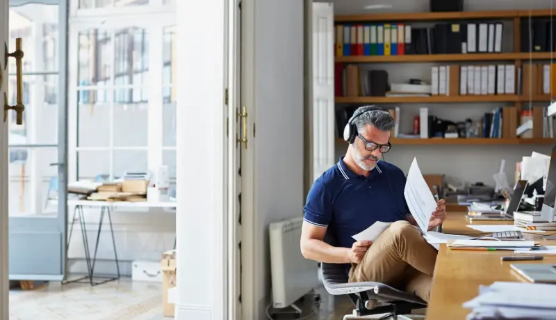 Homme mûr avec des écouteurs assis à un bureau, examinant des papiers.