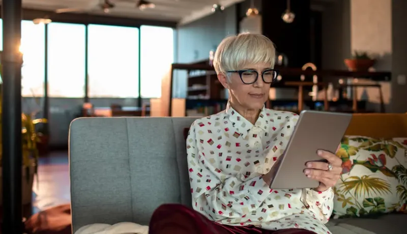 Une femme consulte sa tablette dans son canapé.