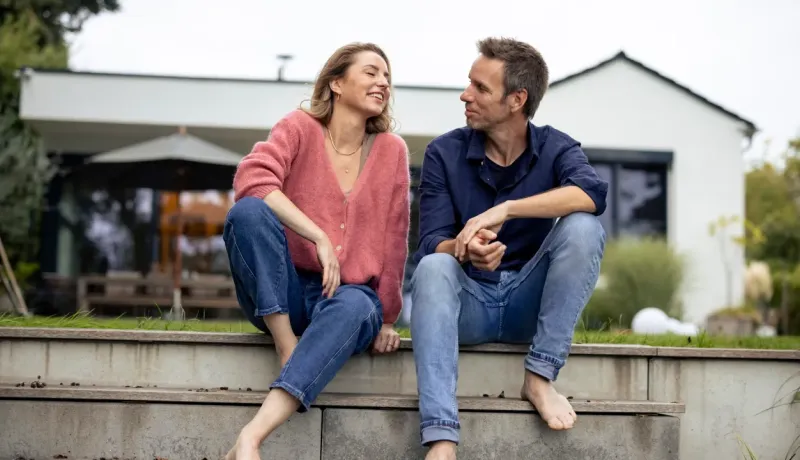 Couple assis sur des marches à l’extérieur, souriants, partageant une conversation.