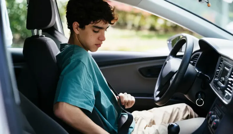 Jeune personne assise sur le siège conducteur d'une voiture, attachant sa ceinture de sécurité.