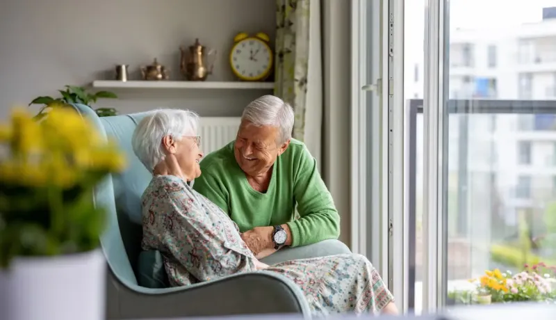 Couple âgé discutant près d'une fenêtre, ambiance chaleureuse.