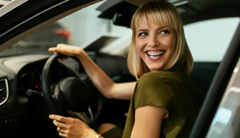 Une femme sourit au volant de sa voiture, heureuse et confiante, prête à partir en déplacement.