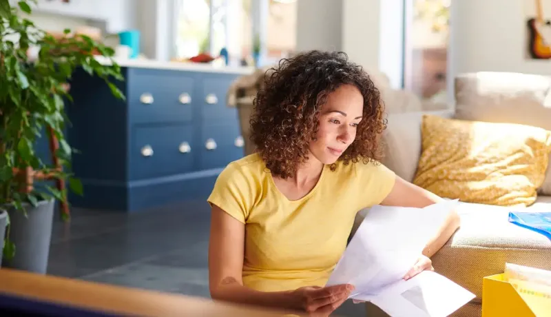 Femme d'âge moyen regarde des documents devant son canapé.