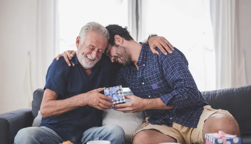 Homme âgé et homme d'âge moyen sont sur le canapé et s'offrent un cadeau.