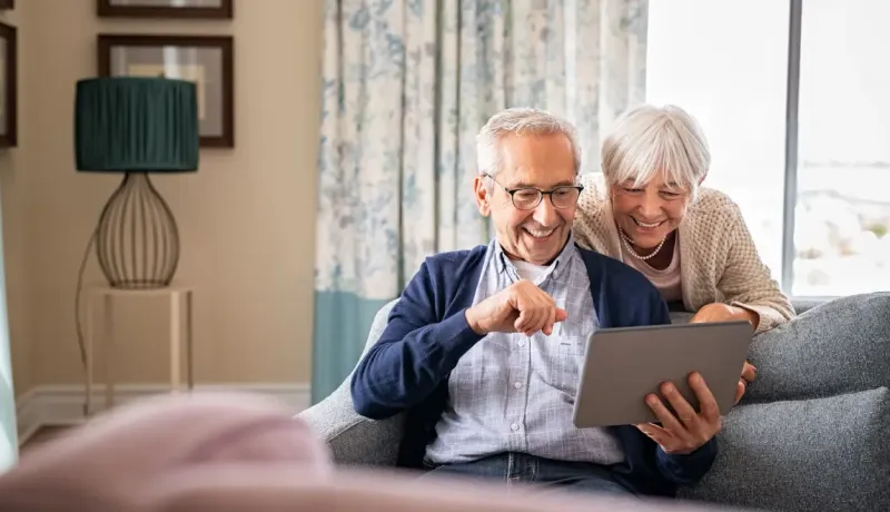 Couple de séniors en train de consulter leur tablette sur leur canapé.