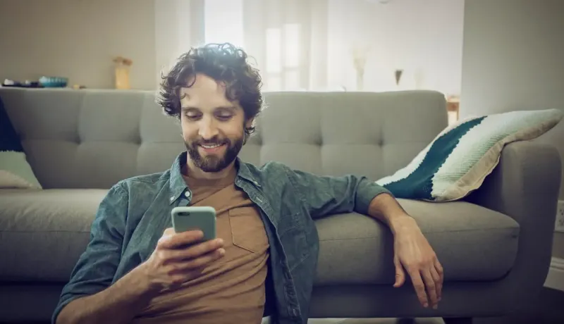 Homme utilise son smartphone devant son canapé.