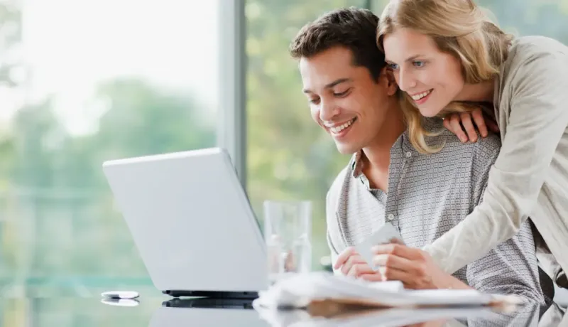 Homme et une femme sourient en regardant un ordinateur sur une table.
