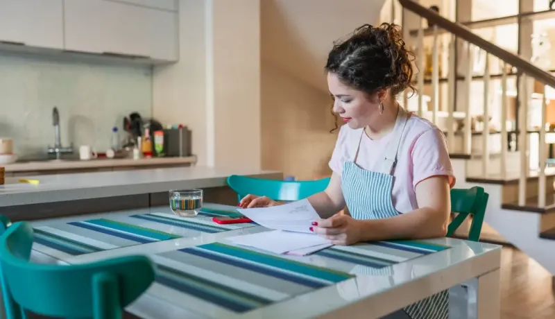 Une femme en train de lire des documents dans sa cuisine.