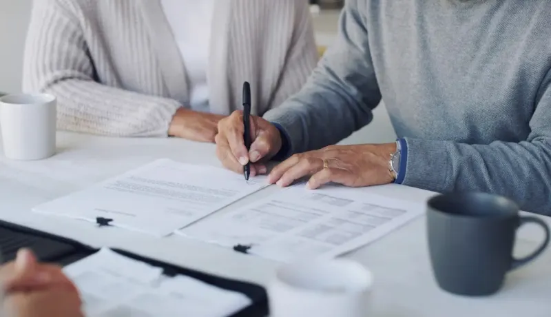 Homme en train de signer des documents en présence de sa femme.
