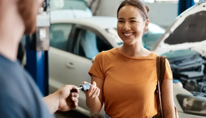 Femme souriante reçoit les clés de sa voiture d'un mécanicien dans un garage.
