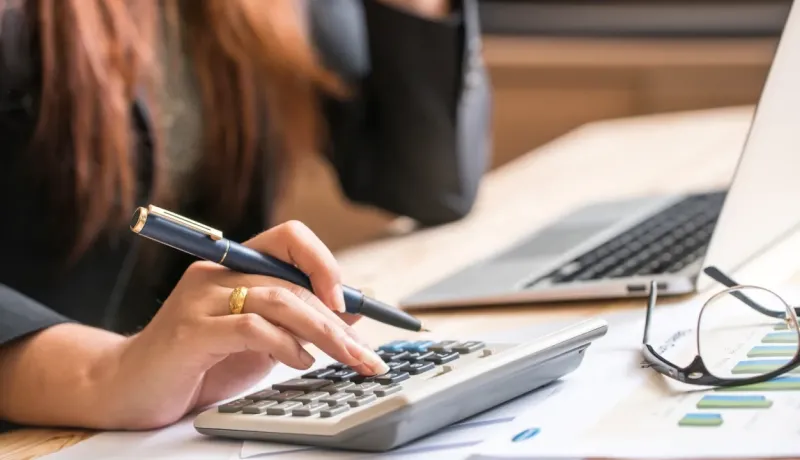 Gros plan d'une main de femme utilise une calculatrice et prend des notes, concentrée sur la gestion de son budget.