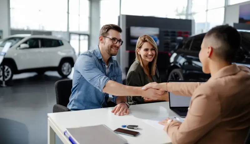 Un vendeur de voitures serre la main d'un client.